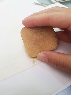 A close up of a conservator removing adhesive using a spongy rubber