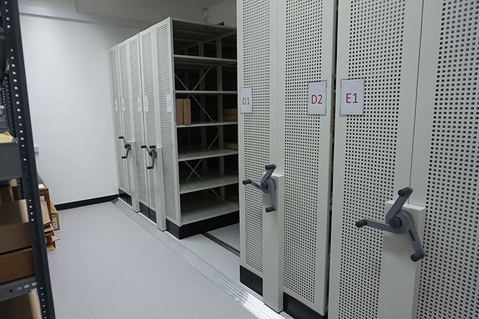 New sorting room - one side of the room is filled with mobile shelving, with handles which turn to move the shelves along. On the opposite side of the room you can see the edge of an open rack of shelves, with some boxes on it.