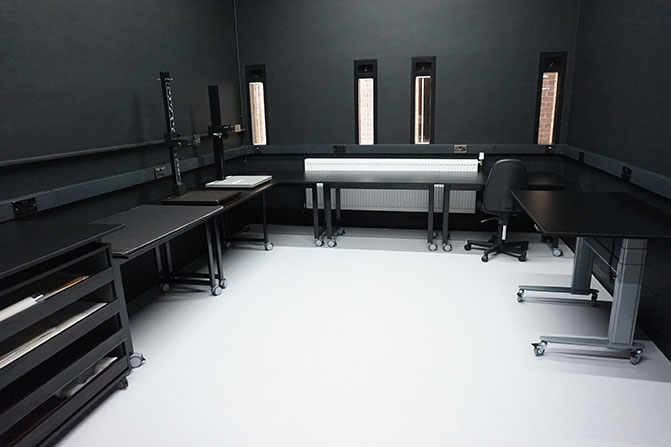 The newly refurbished reprographics room. There are large tables against the three walls, which are painted black. There is a plan chest on the left hand side of the room, and two over head scanners on one of the tables.