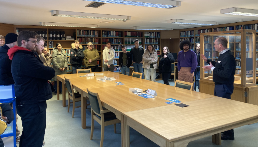 Colour photograph of the Archives Centre reading room, with students standing around 3 tables, while the Director talks to them