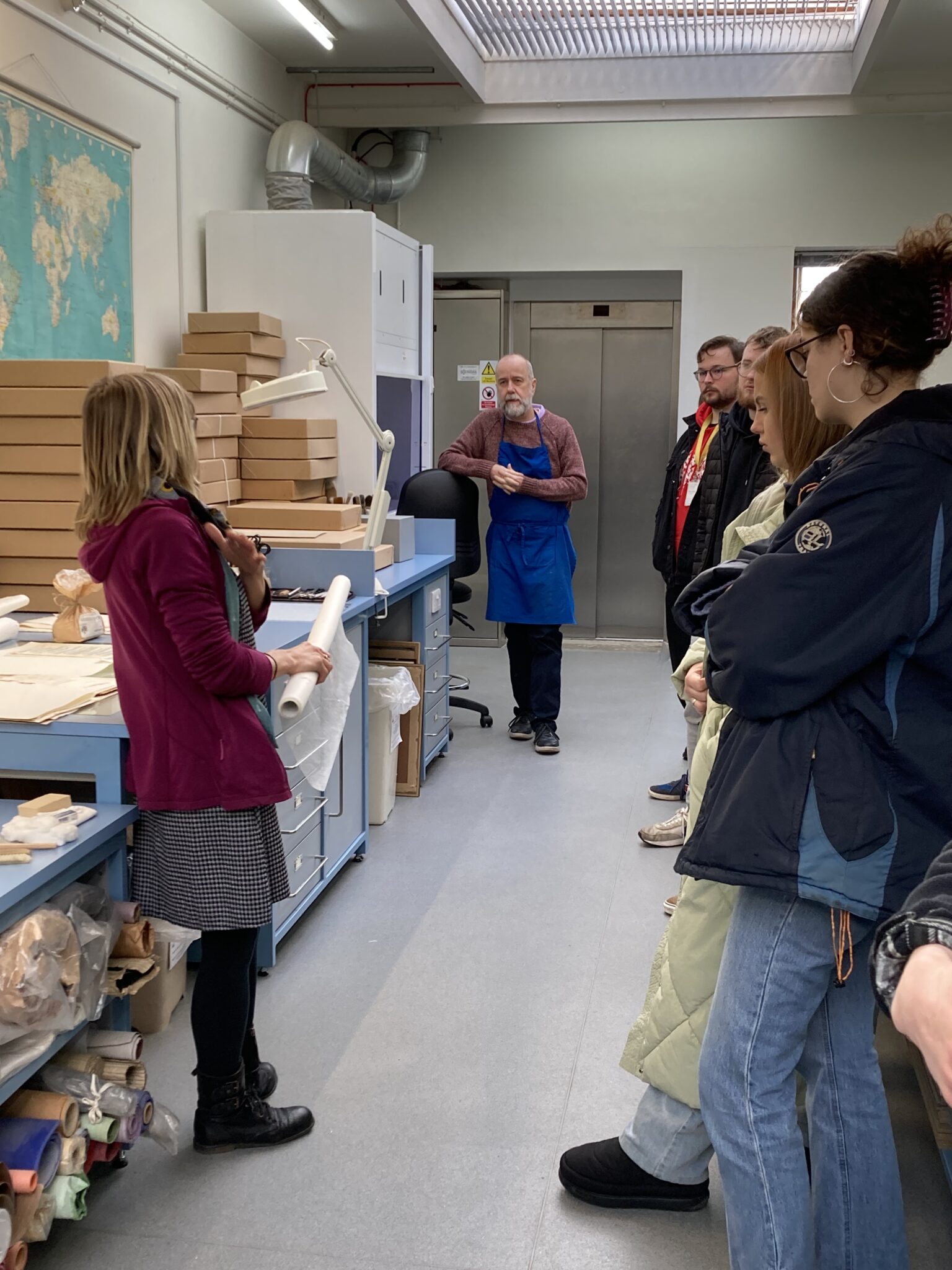 Colour photograph of the conservation lab, with students lined up on one side, and two conservators facing each other, on the other side