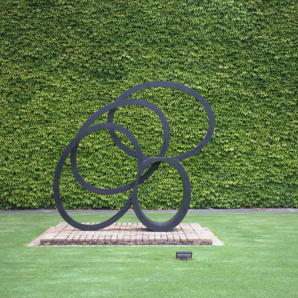 A photograph of Hall's sculpture 'Southern Shade I' against a backdrop of the Squash Courts, Churchill College