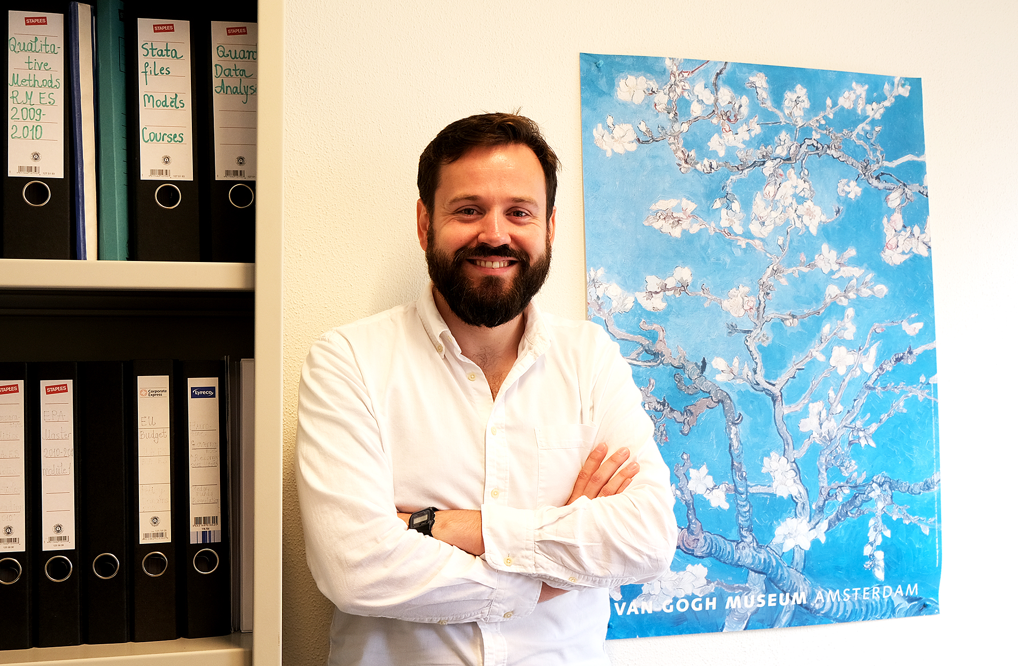 Half length image of Jacob Ward, standing between a Van Gogh poster and a filing cabinet