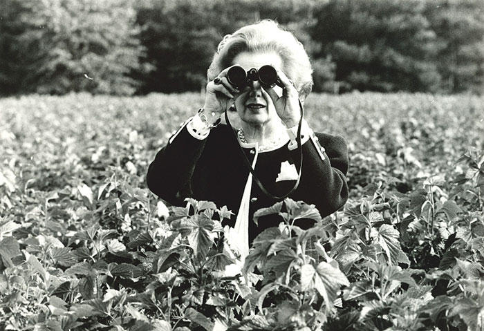 Margaret Thatcher in a field, looking through binoculars