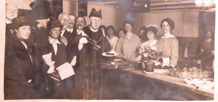 Photograph of the Chelsea national kitchen, with a local dignitary posing with a plate of food beside the kitchen staff